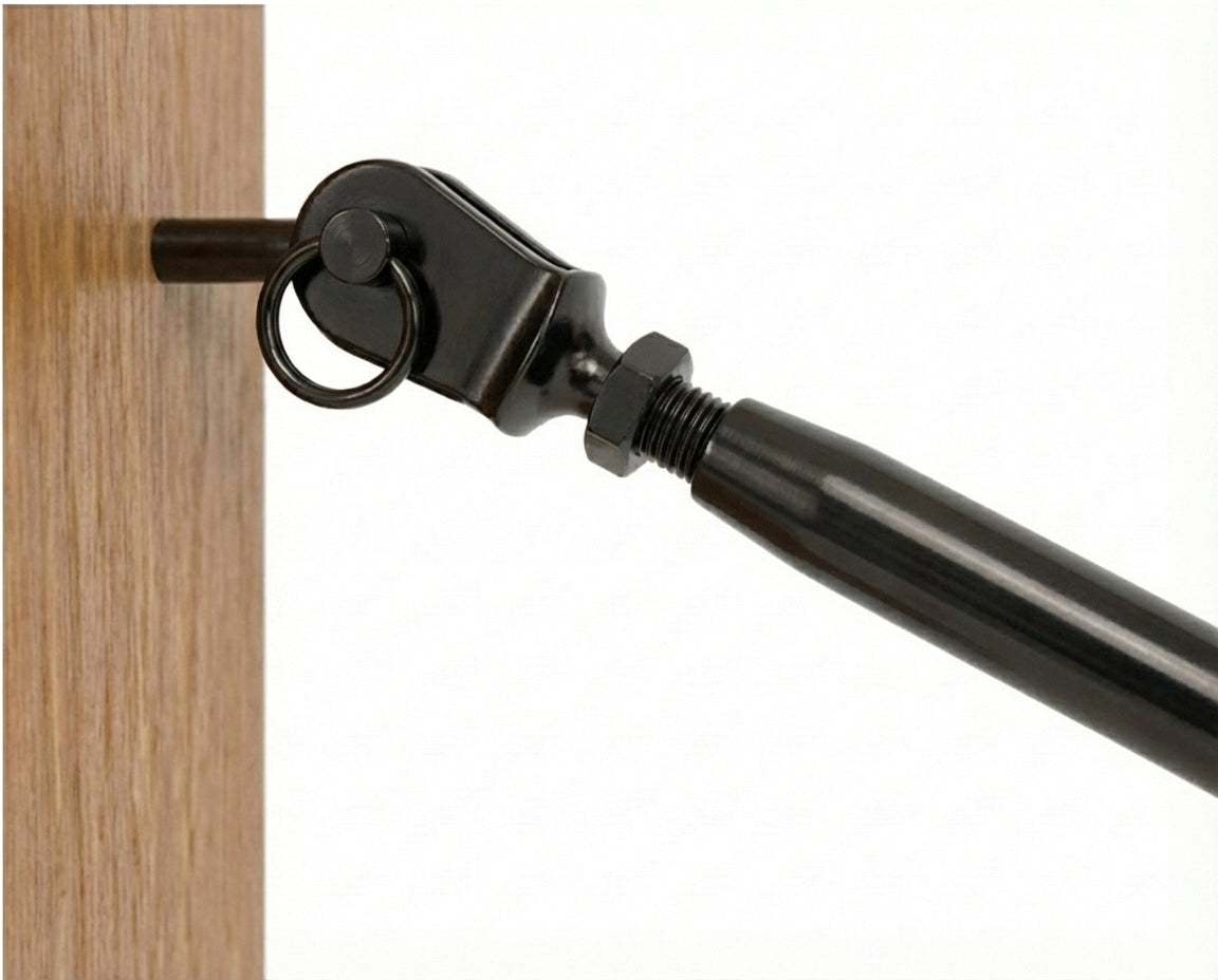 Close-up view of a black cable railing tensioner fitting securely installed into a wooden deck post, holding a taut stainless steel wire rope.
