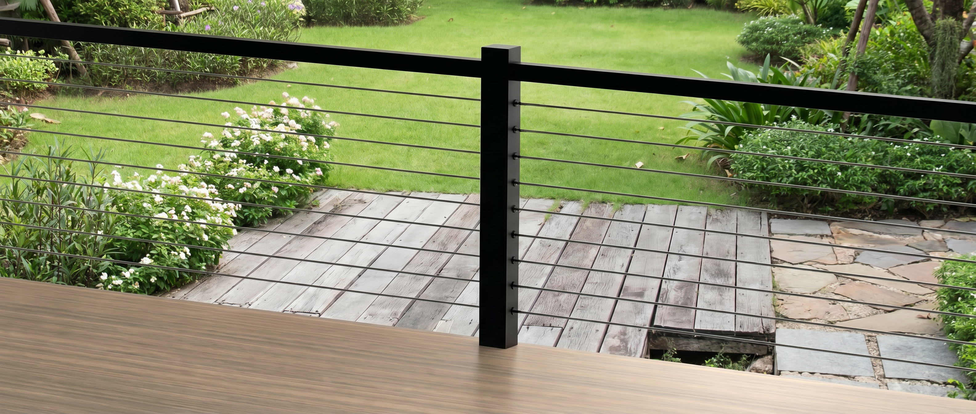 A stylish modern outdoor deck featuring a black metal post cable railing system. The sleek horizontal wire ropes provide a secure barrier while maintaining a perfectly clear and unobstructed view of the lush green backyard garden and stone pathway.
